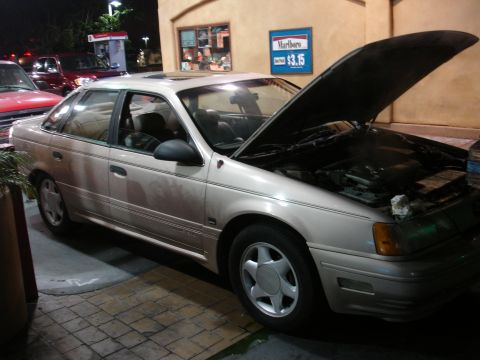 1991 Ford Taurus - A 1991 Ford Taurus sedan is parked with its hood open at a gas station.