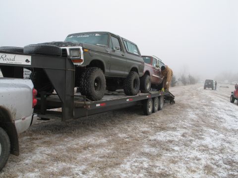 1995 Ford Bronco - A dark green Ford Bronco is loaded onto a trailer with another vehicle behind it on a foggy day.