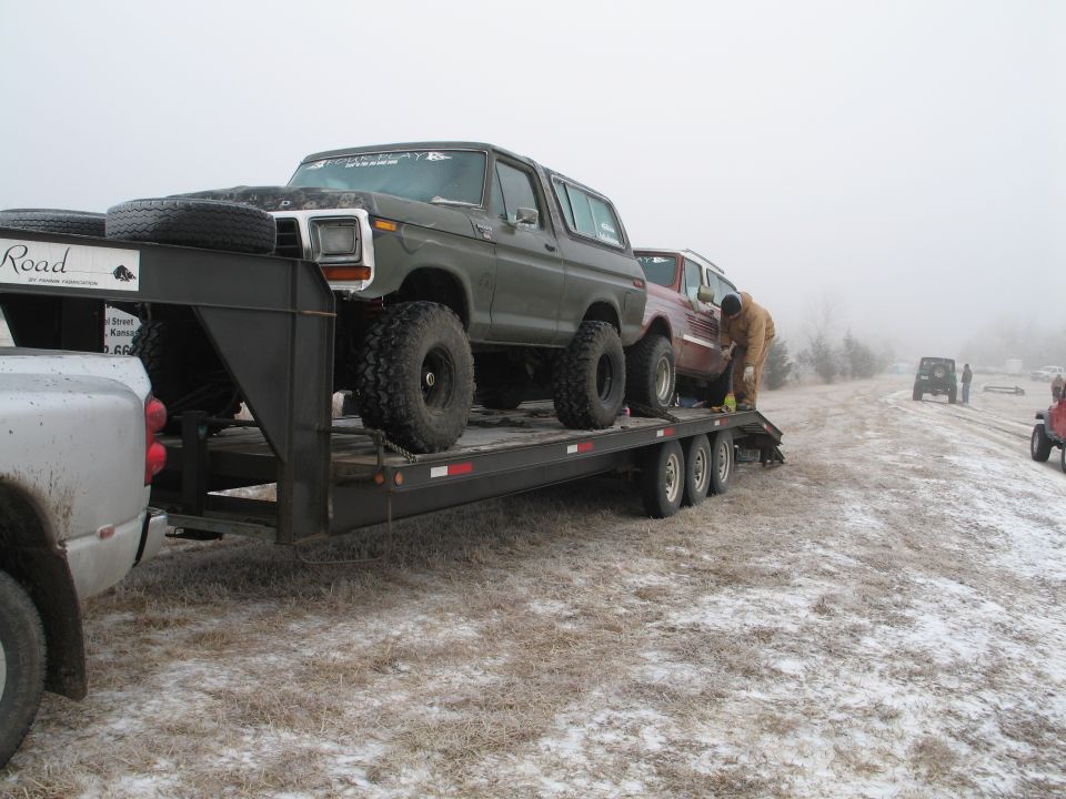 Dark green Ford Bronco on a trailer, lifted with large tires, spare tires on front of trailer