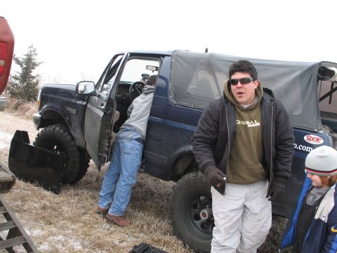 1995 Ford Bronco - A blue 1995 Ford Bronco with a plow attachment and soft top is parked in a field with people around it.
