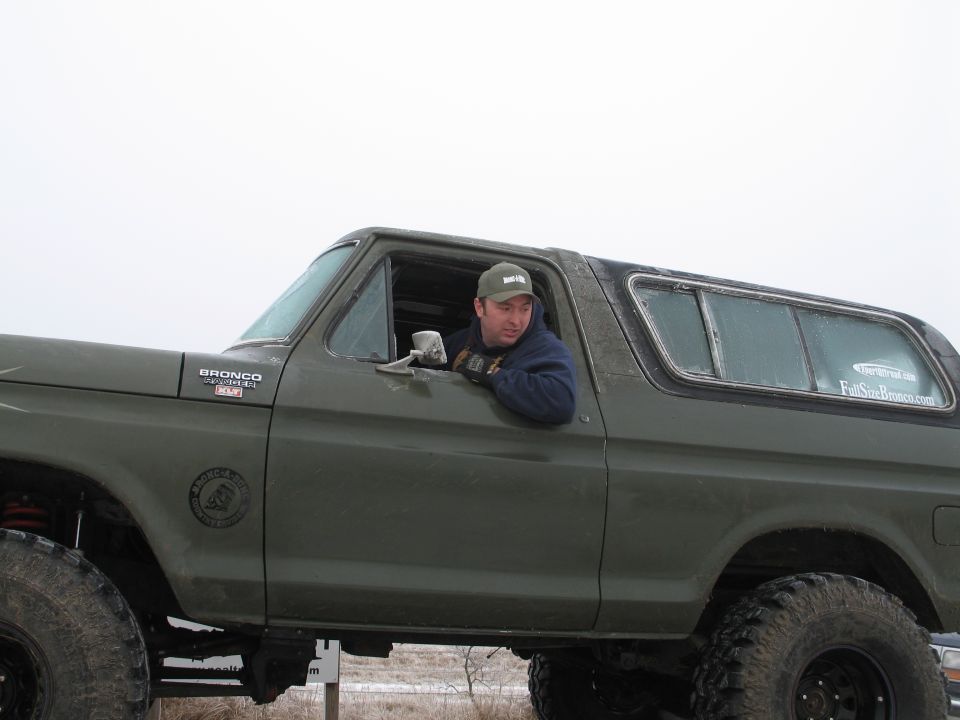 Man wearing a green baseball cap sits in the driver's seat of a lifted green Ford Bronco
