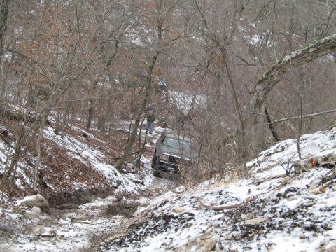 1995 Ford Bronco - An SUV navigates a challenging snowy and muddy trail, with another vehicle following in the distance.