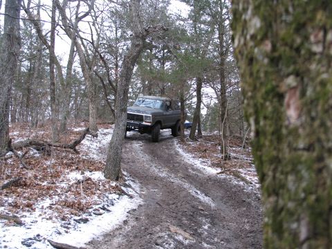 1995 Ford Bronco - A Ford Bronco navigates a challenging off-road trail with patches of snow and mud.