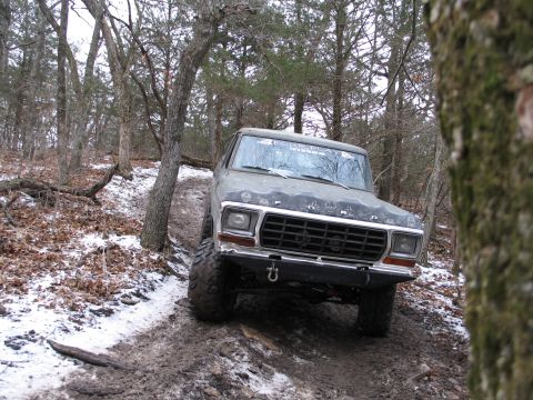 1995 Ford Bronco - This Ford Bronco navigates a challenging off-road path through a wooded area with patches of snow.