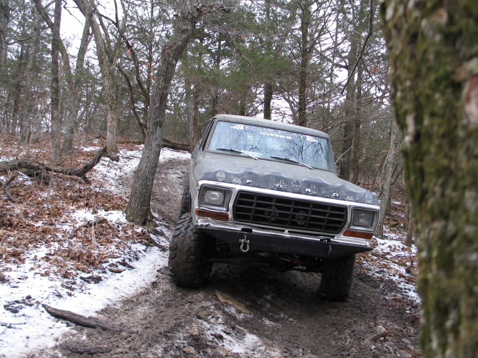 Gray Ford Bronco with off-road tires on a muddy, snowy trail in a forest