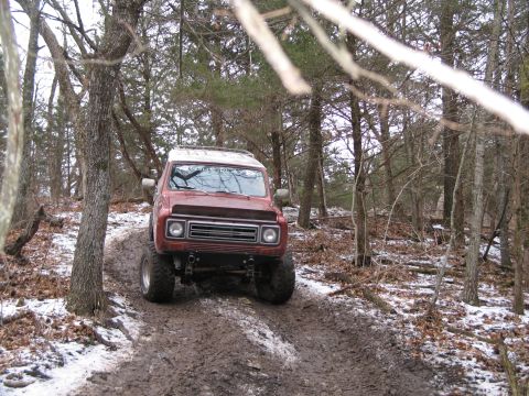 1995 Ford Bronco - A red SUV navigates a muddy and snowy path in a wooded area.