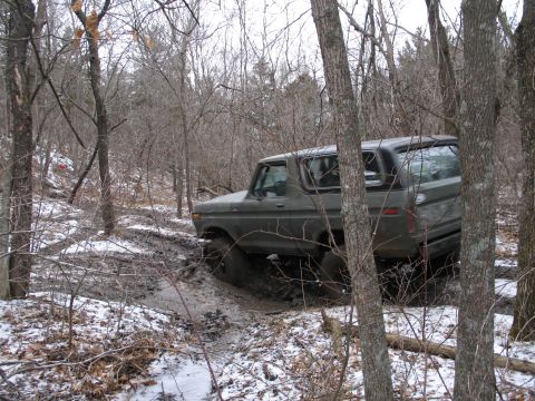 1995 Ford Bronco - This vintage Ford Bronco navigates a challenging muddy trail surrounded by trees in a winter landscape.