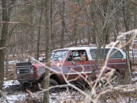 1995 Ford Bronco - A red and white SUV navigates a muddy trail through a wooded area during winter.