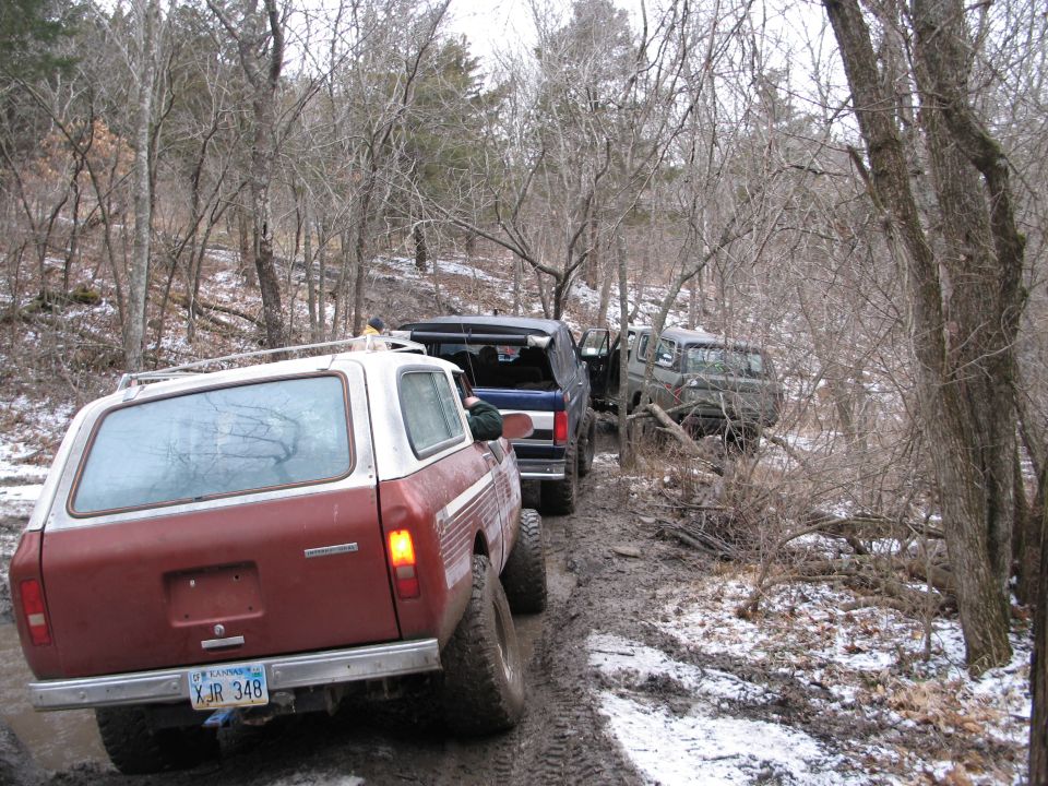 Several off-road vehicles driving on a muddy trail through a wooded area