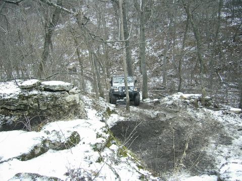 1978 Ford Bronco - A white Jeep Wrangler navigates a muddy and snowy trail through a wooded area.