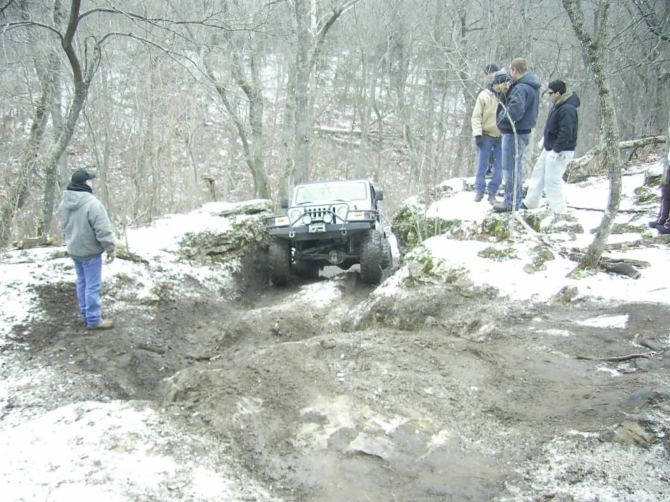 Jeep Wrangler navigating a muddy, snowy trail with onlookers