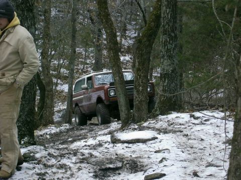 1978 Ford Bronco - A brown SUV with a white top navigates a snowy and wooded trail.