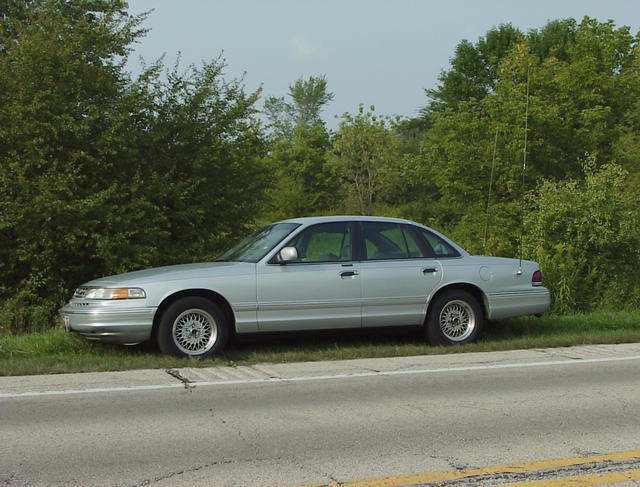 Silver 1996 Ford Crown Victoria parked on the side of the road with trees in the background