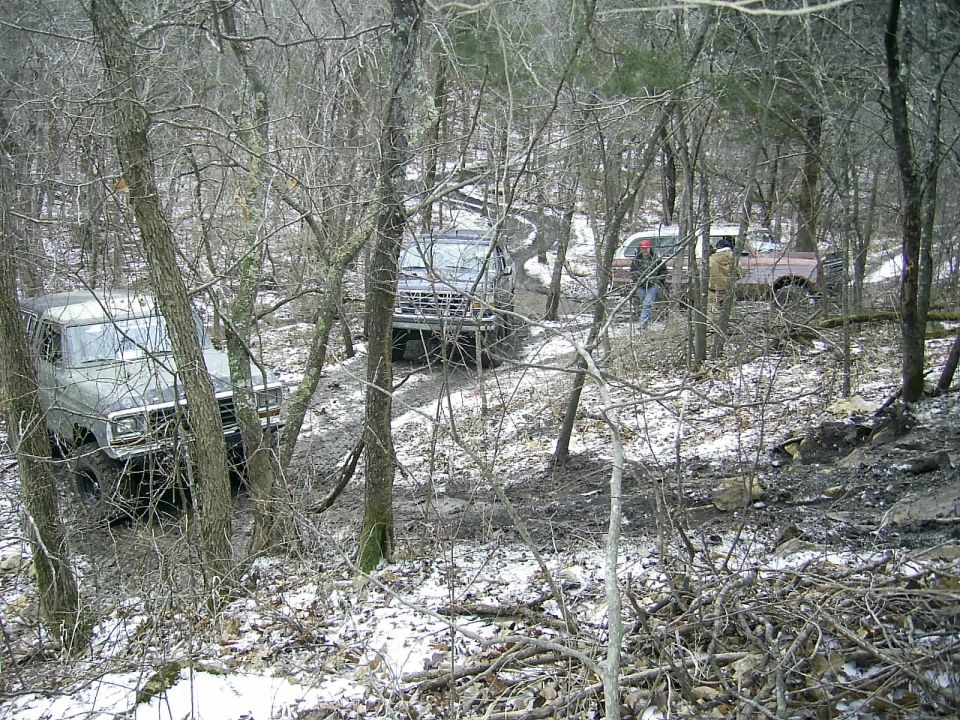 1978 Ford Bronco driving on a muddy trail through trees