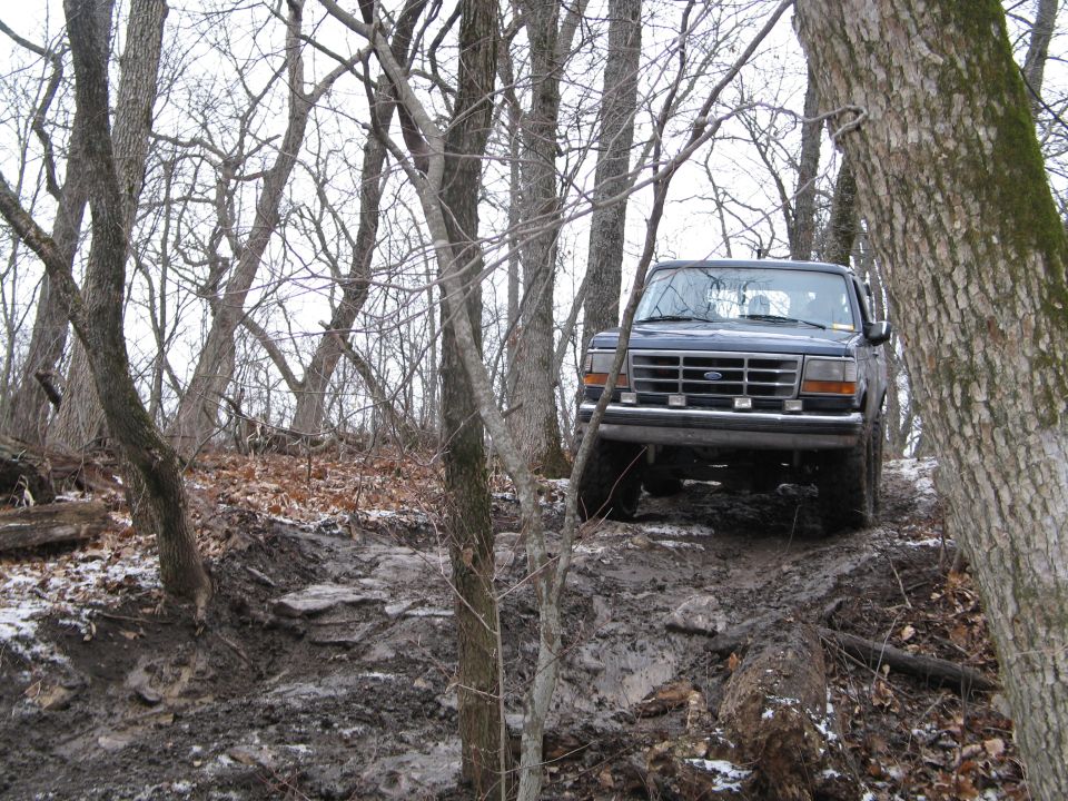 1995 Ford Bronco driving on a muddy, wooded trail