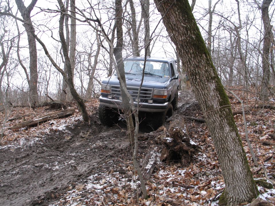 Dark blue Ford Bronco driving on a muddy, wooded trail in winter