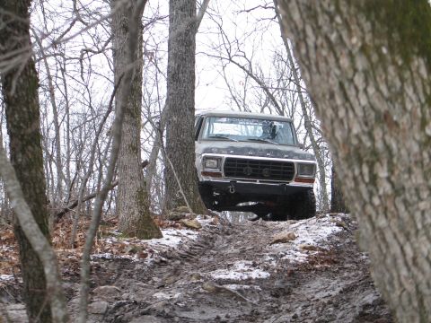 1995 Ford Bronco - A lone gray SUV navigates a wooded path, its front grille visible through the trees.