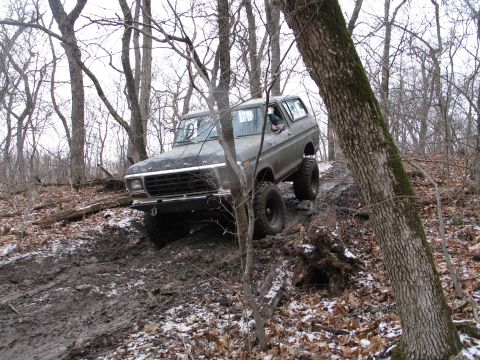 1995 Ford Bronco - Ford Bronco navigates a challenging muddy trail through a forest.