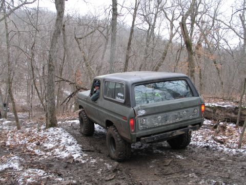 1995 Ford Bronco - This Ford Bronco is navigating a challenging off-road trail with mud and patches of snow.