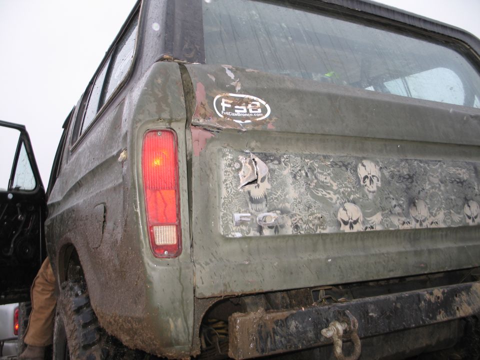 Rear of a green Ford Bronco with skull graphics and an F-8 sticker. The tailgate is damaged