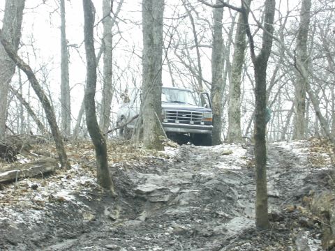 1978 Ford Bronco - A dark gray Ford Bronco navigates a muddy, wooded trail with its door open.