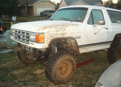 1987 Ford Bronco - Mud-covered 1987 Ford Bronco with a removed front fender and lifted suspension sits in a grassy yard.