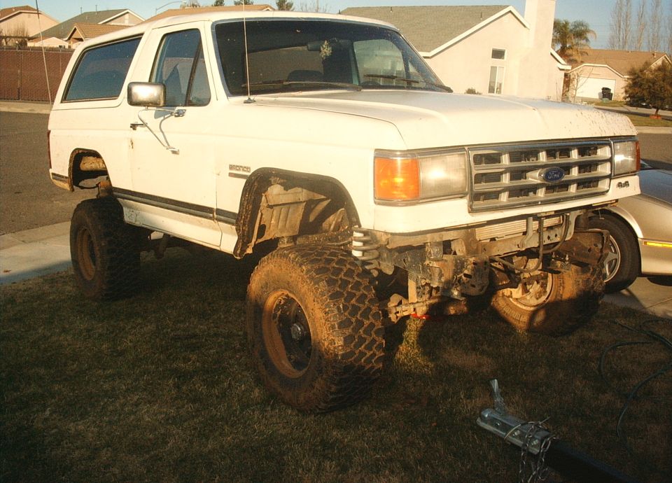 1987 Ford Bronco with lifted suspension, off-road tires, and missing front bumper