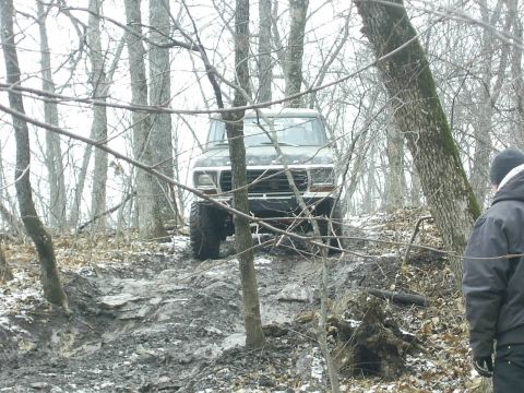 1978 Ford Bronco - A 1978 Ford Bronco navigates a challenging muddy incline in a forest setting.
