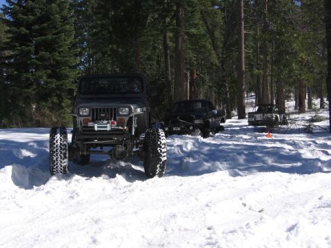 1989 Ford Bronco - A gray Jeep Wrangler navigates a snowy forest road, with two other vehicles in the distance.