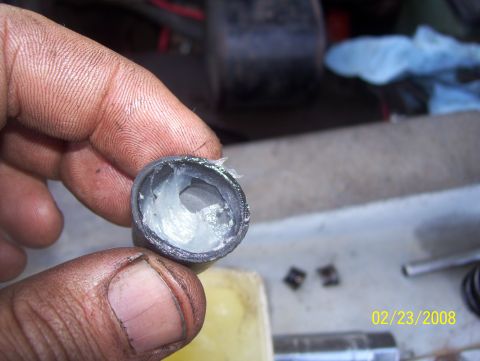 1978 Ford Bronco - A close-up shows a hand holding a metal part packed with grease, with a date stamp and website visible in the background.