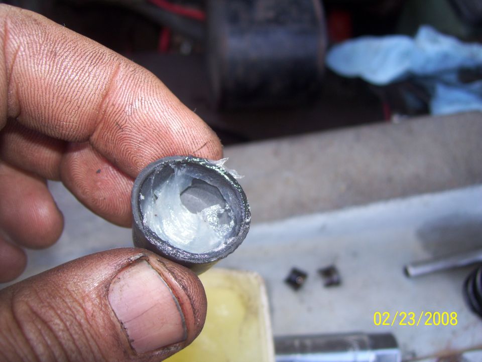 Hand holding a metal part filled with white grease. Date stamp 02/23/2008 and "SUPERMOTORS" logo visible