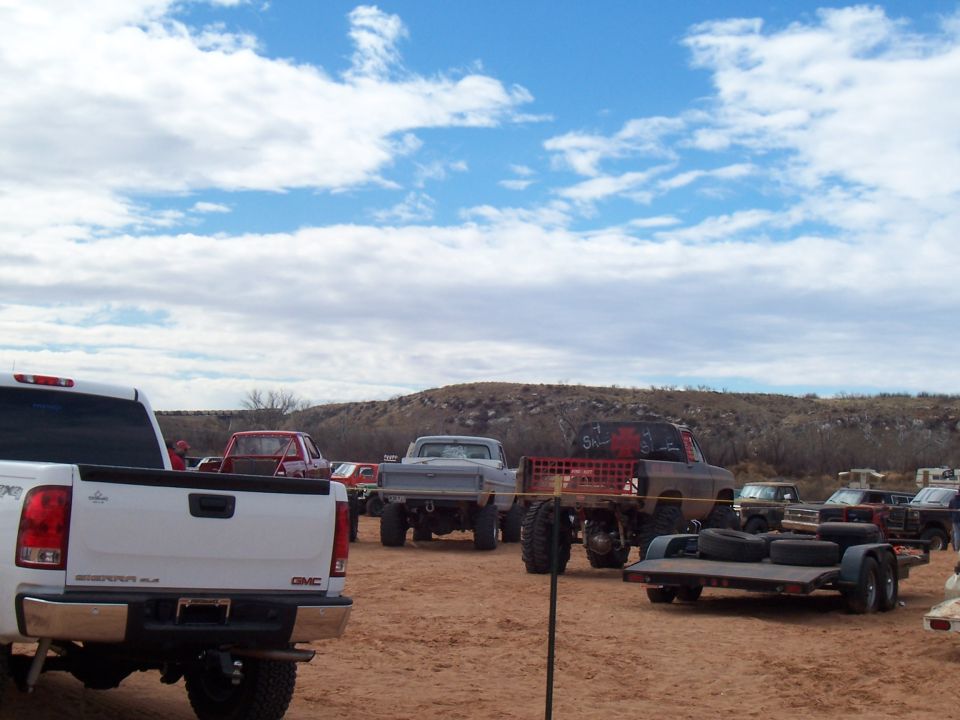 Several modified trucks and trailers parked on a dirt lot under a cloudy sky