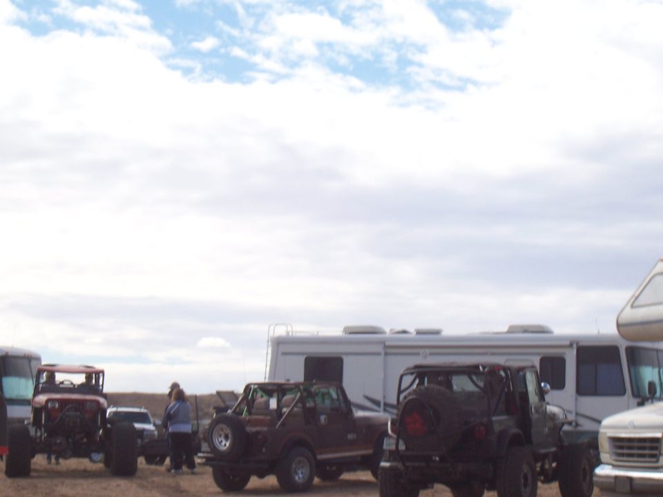 Several modified off-road vehicles parked near RVs under a cloudy sky