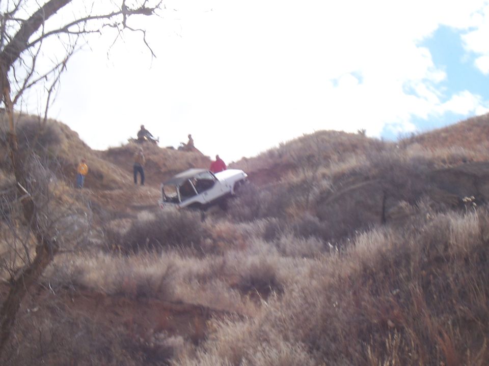 White off-road vehicle tilted on a muddy hillside with people watching