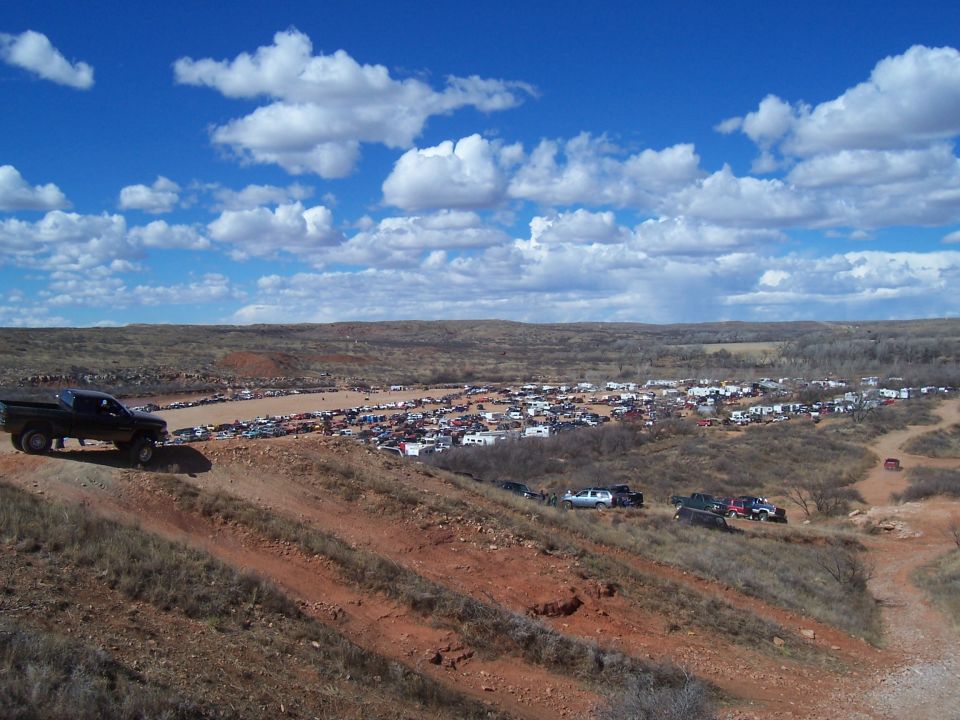 Truck on a dirt hill overlooking a large gathering of vehicles in a valley below