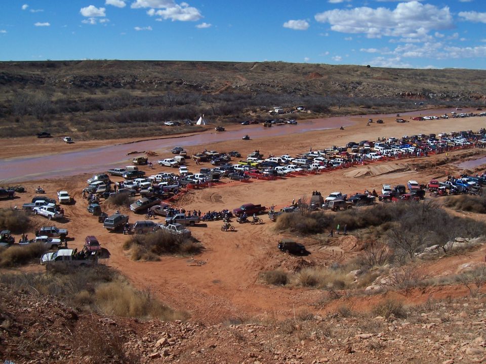 Many vehicles parked along a muddy riverbed with people gathered