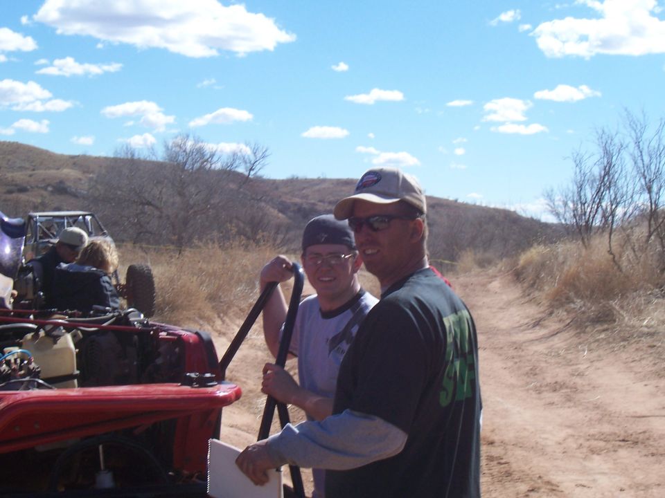 Red off-road vehicle with open hood and purple buggy in background on a dirt road