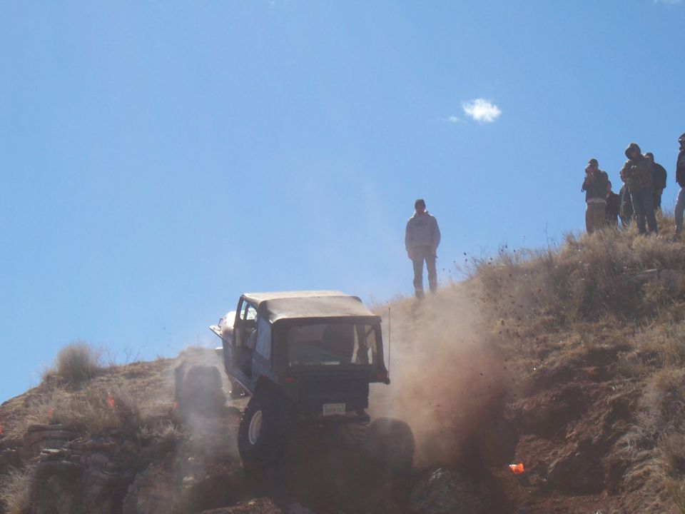 Dark off-road vehicle with a soft top climbing a dusty hill, seen from the rear