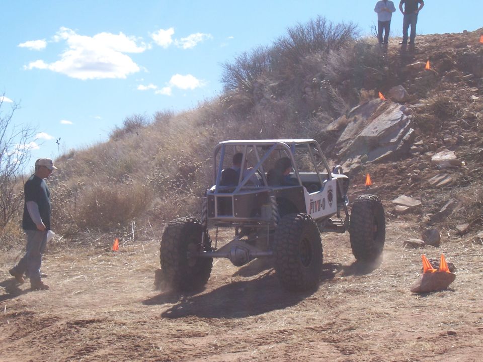 Rear view of a custom off-road buggy with large tires and a roll cage, navigating a dirt course