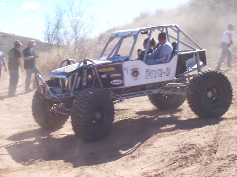 Off-road buggy with a roll cage, large tires, and "FIVE-O" text on the side, driving on a dirt track