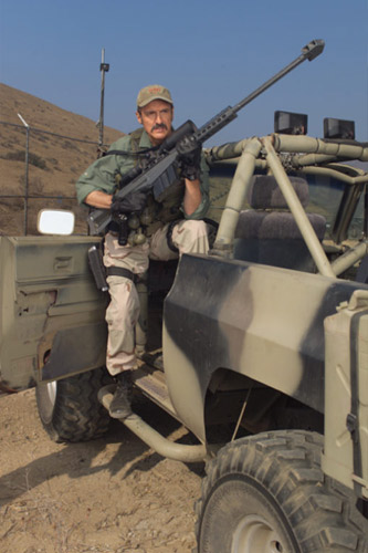 1989 Ford Bronco - Man with sniper rifle poses in a camouflaged military vehicle.