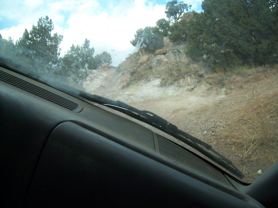 View from inside a vehicle looking out at a dirt road going uphill through rocky, scrubby terrain