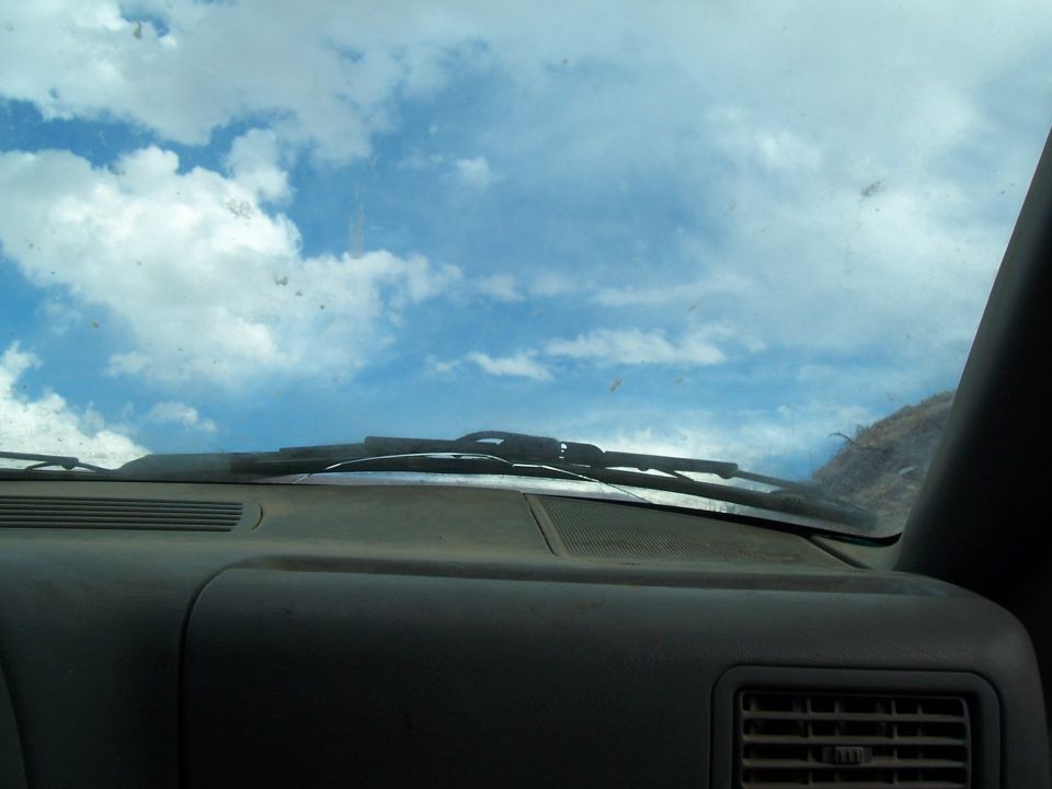 view from inside car, looking at dashboard and windshield with clouds in the sky