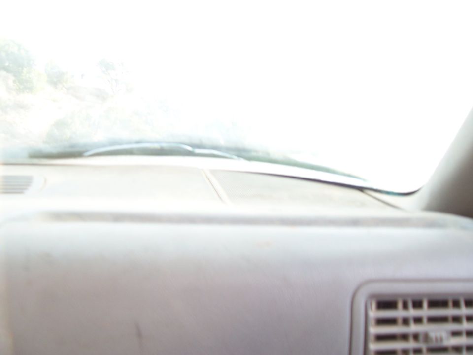 View from inside a car, looking at the dashboard and windshield. Bright light outside