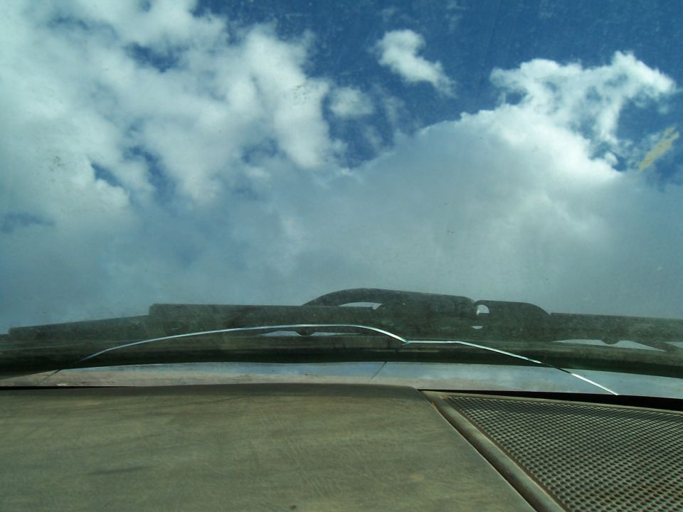 View from inside a car, looking out the cracked windshield at clouds. Dashboard is visible