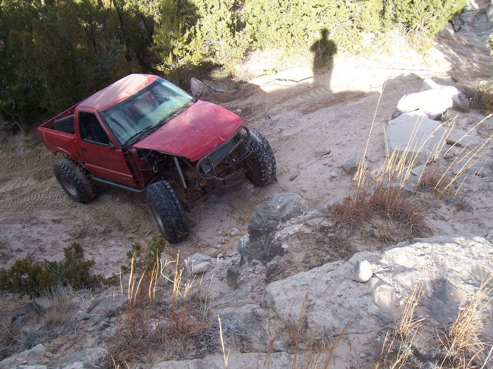 Red pickup truck with modified suspension and off-road tires navigating a rocky, sandy terrain
