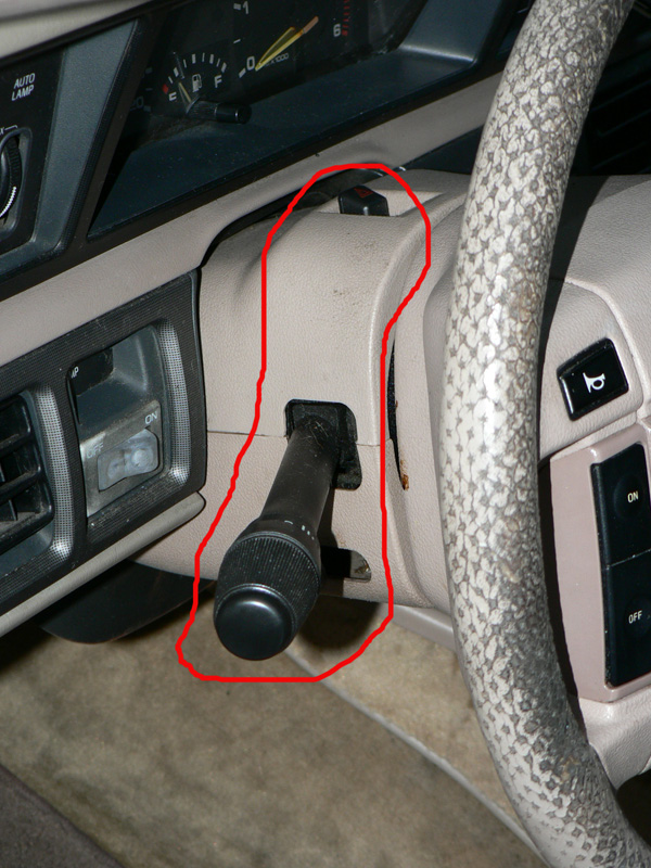 Turn signal stalk on tan steering column circled in red inside a car with gray wheel cover