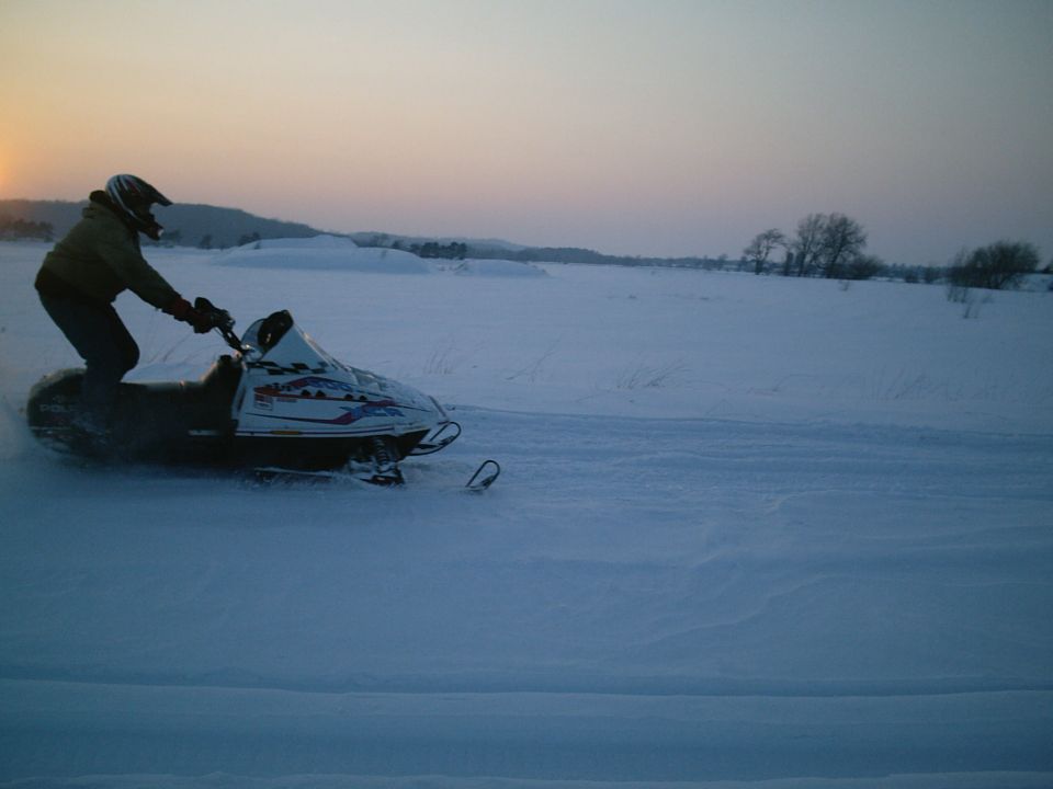 Rider on white Polaris snowmobile crossing snowfield at dusk