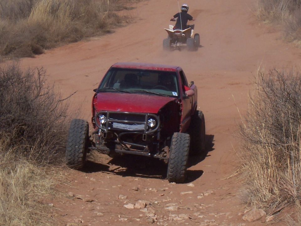 Red off-road pickup truck with custom bumper and exposed engine bay, followed by a quad bike