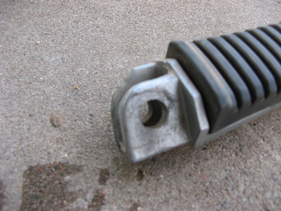 Close-up of a motorcycle foot peg with a rubber grip, resting on concrete